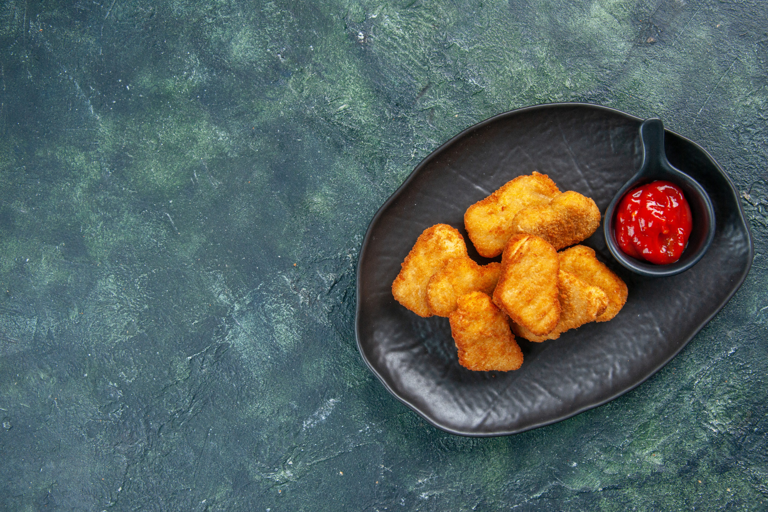 tasty-chicken-nuggets-and-ketchup-in-black-plate-on-the-left-side-on-dark-surface